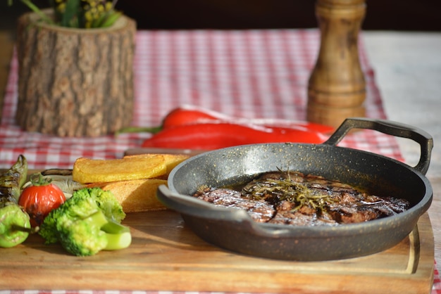 Closeup of deliciously roasted steak in a pan on a board with vegetables on it