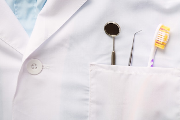 Foto primo piano dello strumento dentale, spazzolino da denti e uno specchio in tasca bianca uniforme medica.