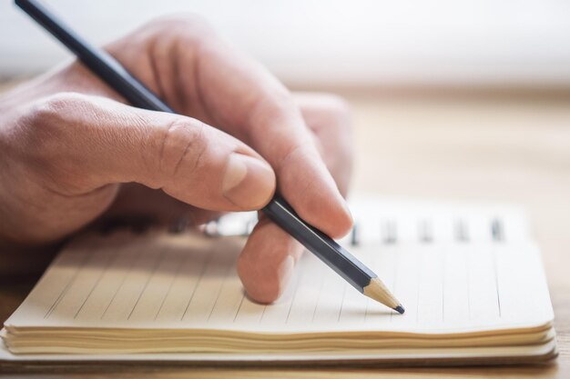 Foto rappresentazione in primo piano della mano di un uomo che prende appunti in un blocco note con uno sfondo sfocato