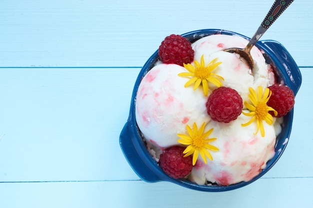 Closeup detail view on ice cream in a blue ceramic bowl. with raspberries, yellow flowers an syrup on top and cute small spoon . flat lay portrait vertical shot