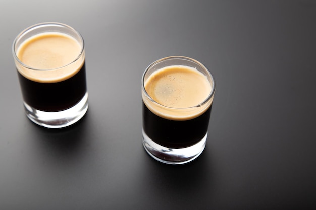 Closeup detail view of two espresso shot glass over shiny elegant black backdrop with copy space