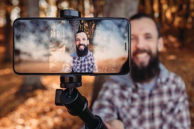 Closeup of digital screen with man over autumn landscape Male tourist using smartphone camera to take selfie in nature park