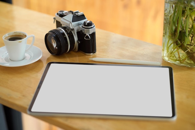 Closeup Digital tablet computer white screen mockup on wooden table with retro camera and coffee cup