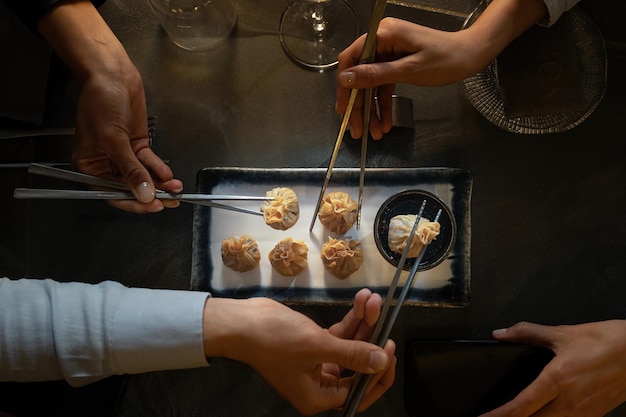 Foto primo piano su dim sum, cibo cinese disposto su un piatto con un gruppo di mani di amici che tengono le bacchette.