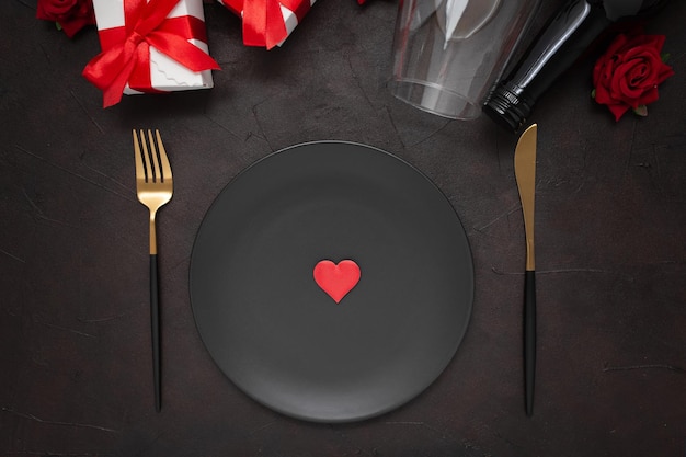 Closeup of a dinner plate, knife, fork, wine bottle, wine glass, gifts, and roses