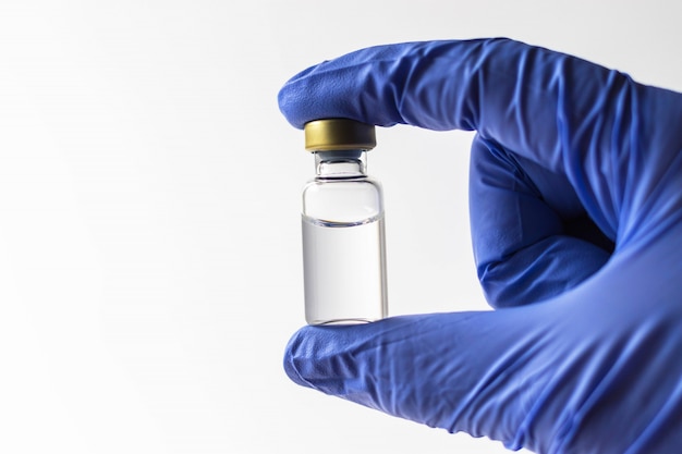 Closeup of doctor hand in blue glove holding vial with liquid for medical injection