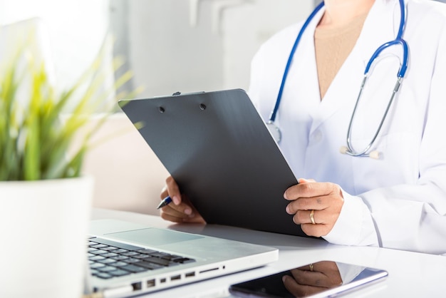 Closeup of doctor or nurse woman in uniform with stethoscope writing information of patient prescription in paperwork