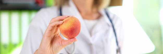 Closeup of doctor nutritionist holding ripe peach in hand healthy food diet vitamins and