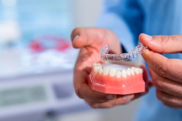 Closeup The doctor puts transparent aligners on the teeth of the artificial jaw