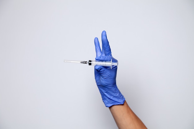 透明な注射器を保持しているゴム製の紫色の手袋で医者の手のクローズアップ