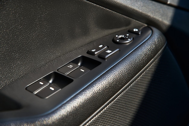 Closeup of a door control panel in a new car. arm rest with\
window control panel, door lock button, and mirror