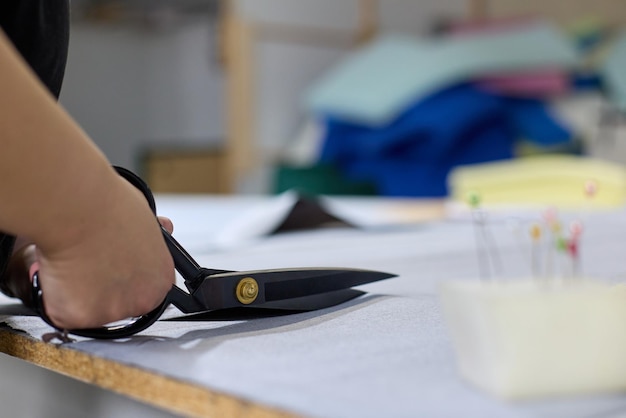 Closeup of dressmaker cutting piece of fabric with scissors in sewing workshop