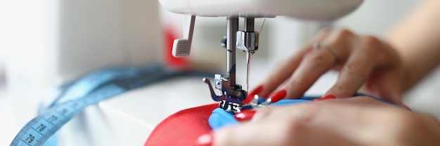 Closeup of dressmaker lady working on white sewing machine professional seamstress creating red
