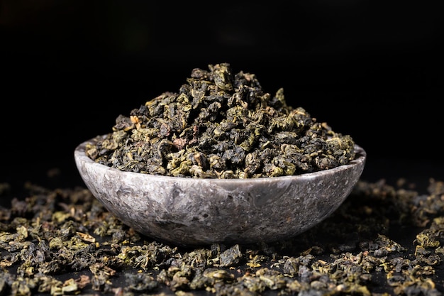 Closeup of dried green tea leaves into black bowl on black background