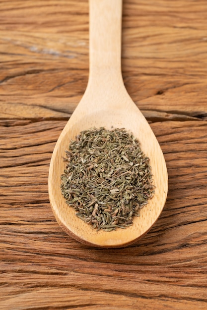 Closeup of dried thyme on a spoon over wooden table.