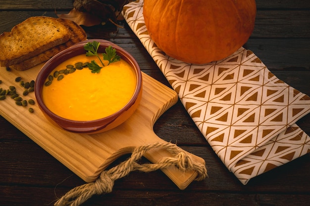 Closeup on a earthenware bowl with a creamy pumpkin soup served with pumpkin seeds and croutons wooden cutting board Vegan vegetarian soup Dark wooden table