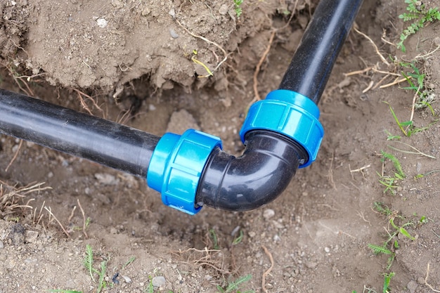 Closeup of elbow fitting and black pvc pipes at bend in trench outdoors plumbing water drainage