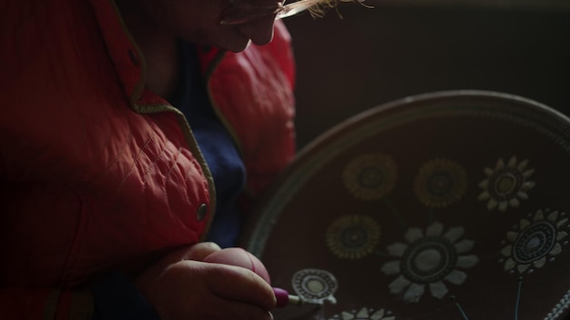 Closeup elderly woman painting plate in studio Portrait of senior lady drawing flower on plate in workshop Focused female artist decorating clay product in pottery