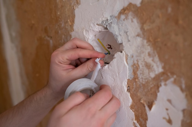 Closeup of an electrician putting two cables together and adding insulating tape on them