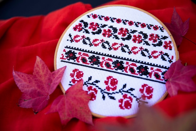 Photo closeup of an embroidery of flowers and an ornament in a frame on a red background among the leaves embroidered with a cross in black and red threads macro