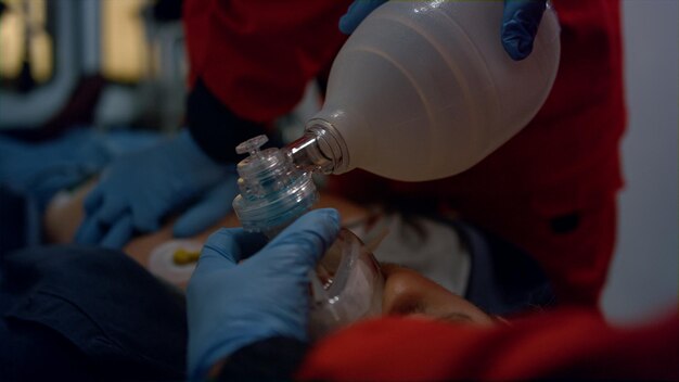 Photo closeup emergency medical doctors hands doing cpr procedure of patient on stretchers ems paramedics ventilating man lungs with respiratory mask medical team treating victim in emergency car