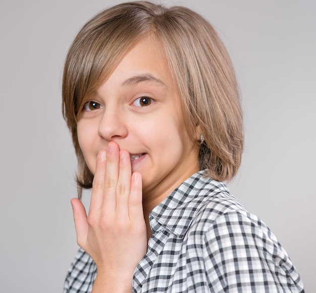 Photo closeup emotional portrait of caucasian girl hand covering her mouth feels fright shock on a gray background amazed child is afraid of fear