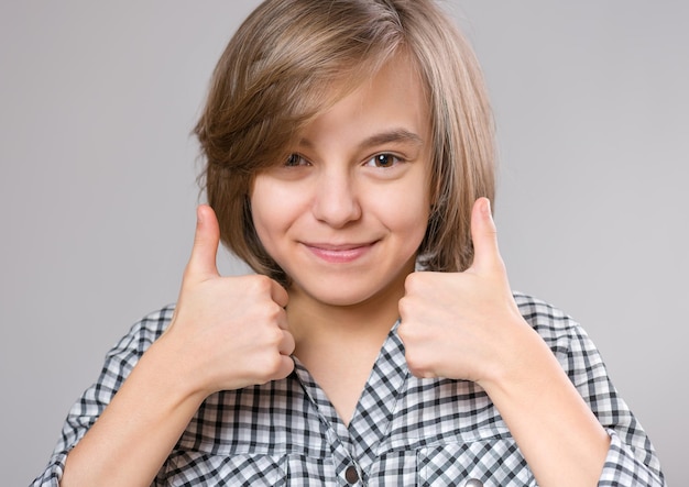 Closeup emotional portrait of caucasian little girl Funny kid making thumbs up gesture on gray background Beautiful child laughing looking very happy