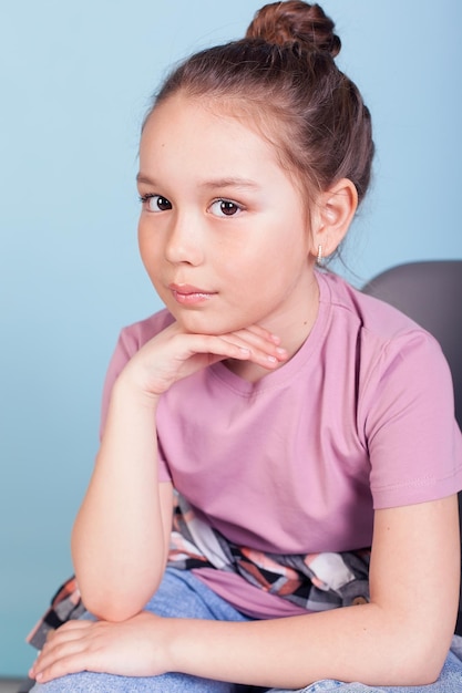 Closeup of an emotional portrait of a cute little girl in a blue shirt on a gray background in the studio She holds her cheeks and smiles