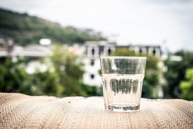 Closeup empty shabby old glass with limescale textured bamboo\
wooden surface table mat on balcony nature green houses city view\
background dehydration alcoholism quitting bad habits\
addictions