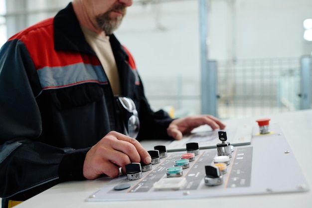 Closeup of engineer in uniform pushing buttons on machine during his work in factory