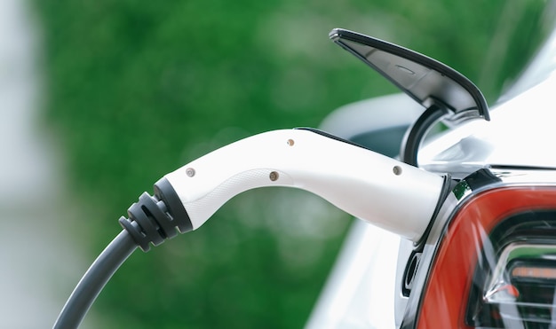 クローズアップ EV 充電器プラグ ハンドルが電気自動車ポートに取り付けられ、充電ステーションからバッテリーを充電中 モダンなデザインの EV 車と、より良い未来のためのクリーン エネルギーの持続可能性 パノラマ シンクロノス