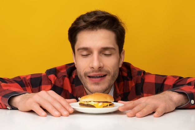 Closeup of excited guy smelling tasty burger at studio