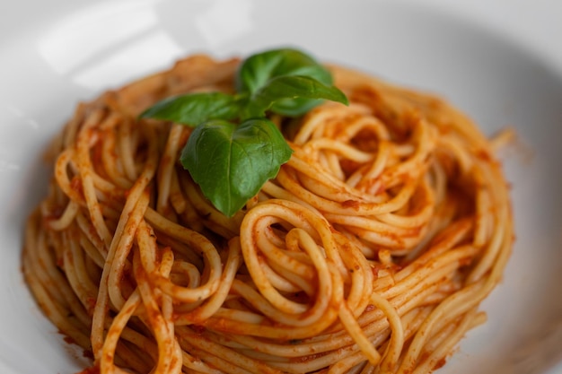 Photo closeup of exquisite pasta adorned with a single basil leaf in a beautiful white pasta bowl