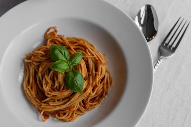 Photo closeup of exquisite pasta adorned with a single basil leaf in a beautiful white pasta bowl