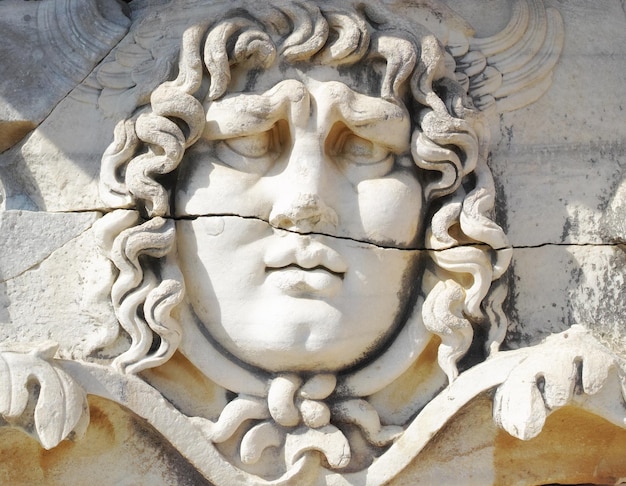 Крупный план лица, вырезанного на мраморе в классическом стиле древними греками в храме Аполлона в Дидиме. Впечатляющее разрушенное святилище или статуя в греческом городе Милет на юго-западе Турции.