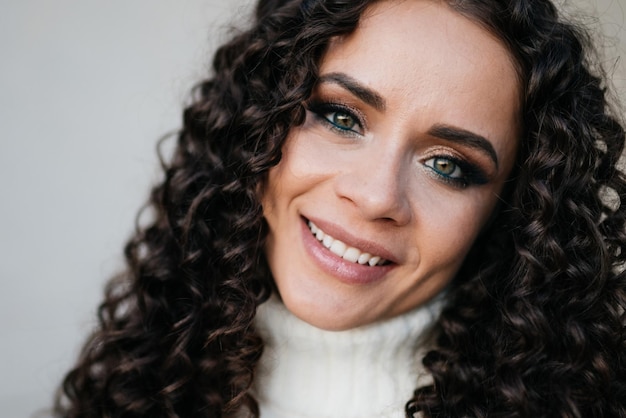 Closeup face curly brunette with white flat teeth and green eyes smiling at the camera