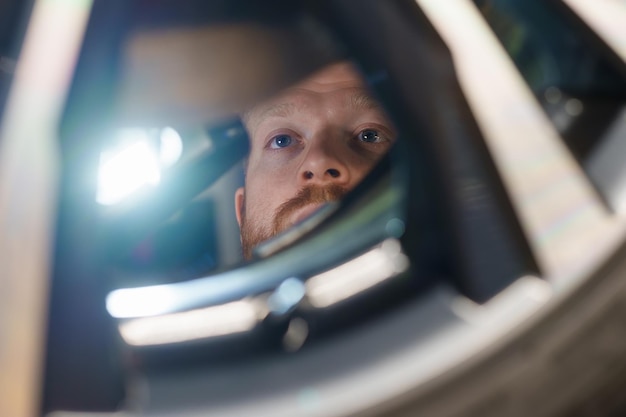 Крупный план лица автомеханика-мужчины, который осматривает тормозную систему автомобиля с фонариком на станции технического обслуживания