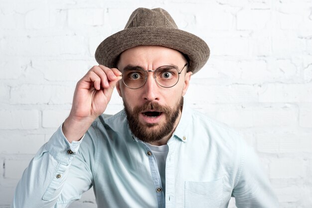 Photo closeup face portrait of bearded man in the hat and glasses looking. emotion surprise, indignation