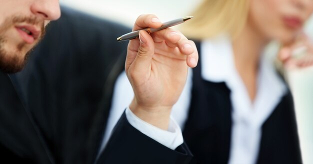 Closeup face of a serious businessman hand with a pen in hand on the background of business team