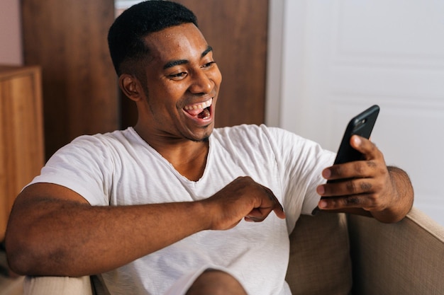 Крупным планом лицо удивленного афроамериканца, получающего хорошие новости с помощью мобильного телефона дома