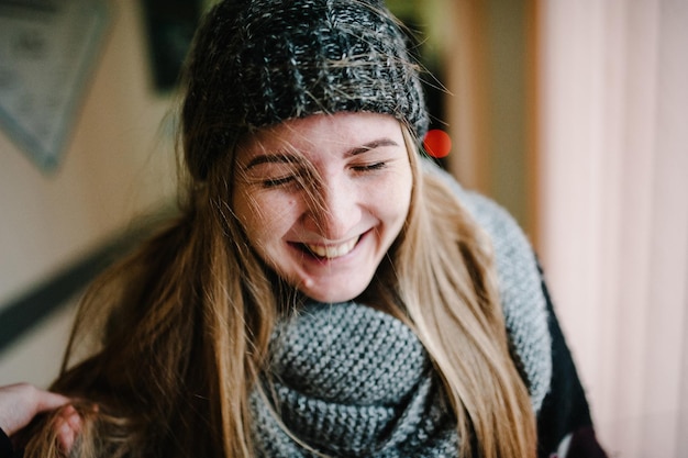 Closeup face of a young happy woman enjoying winter wearing scarf, cap. Smiling girl with closed eyes. Woman with knitted woolen  grey hat and scarf. The wind waves the hair in different directions.