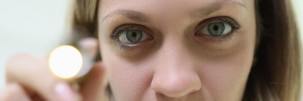 A closeup face of a young woman with a flashlight medical diagnostics ophthalmological study