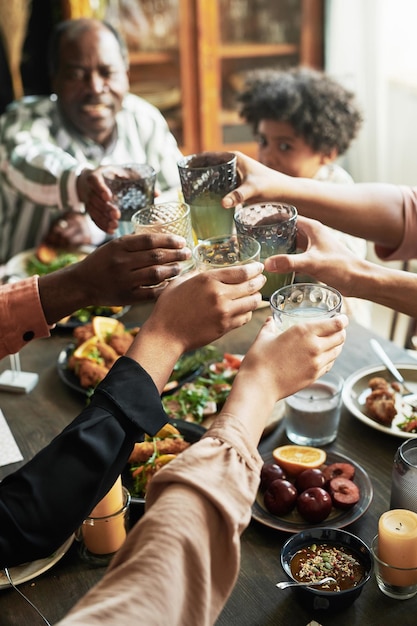 Photo closeup of family toasting with glasses of drinks while sitting at dining table during dinner