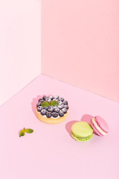 Primo piano di crostate da dessert di mirtilli freschi gourmet fantasia e macarons francesi su rosa. foto di alta qualità