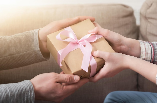 Крупным планом руки отца дарит дочери подарок на день рождения с розовой лентой
