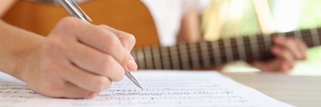 Foto close-up di una compositrice che scrive note musicali in un quaderno mentre un musicista compone musica