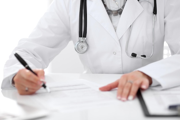 Closeup of a female doctor filling out application form sitting at the table in the hospital