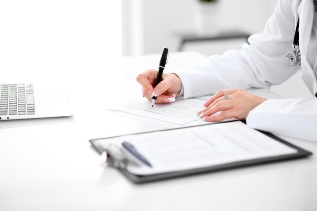 Closeup of a female doctor filling out application form sitting at the table in the hospital