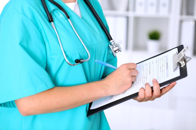 女性医師のクローズアップは、申請書または病歴に記入しています