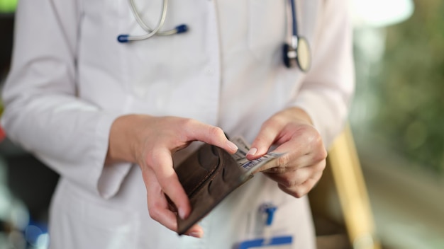 Closeup of female doctor putting cash banknotes in wallet medical staff salary bribe or paid